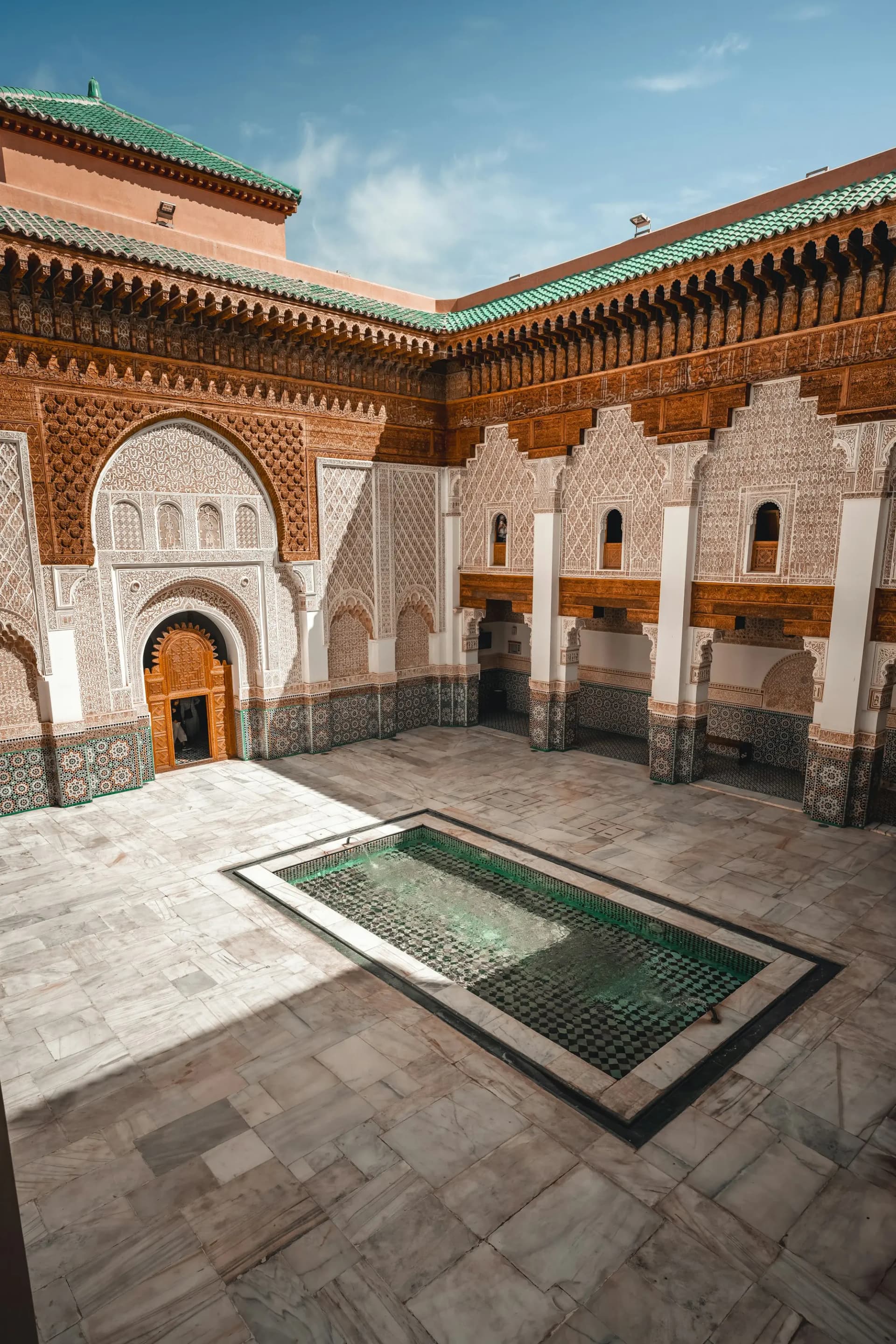 Carved stucco and zellige tilework around a courtyard fountain in a historic Marrakech building